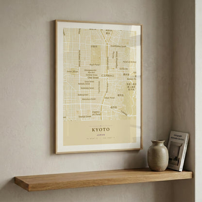 A framed vintage-style map print of Kyoto, Japan, hanging on a textured beige wall above a wooden floating shelf with a ceramic vase and a small book.