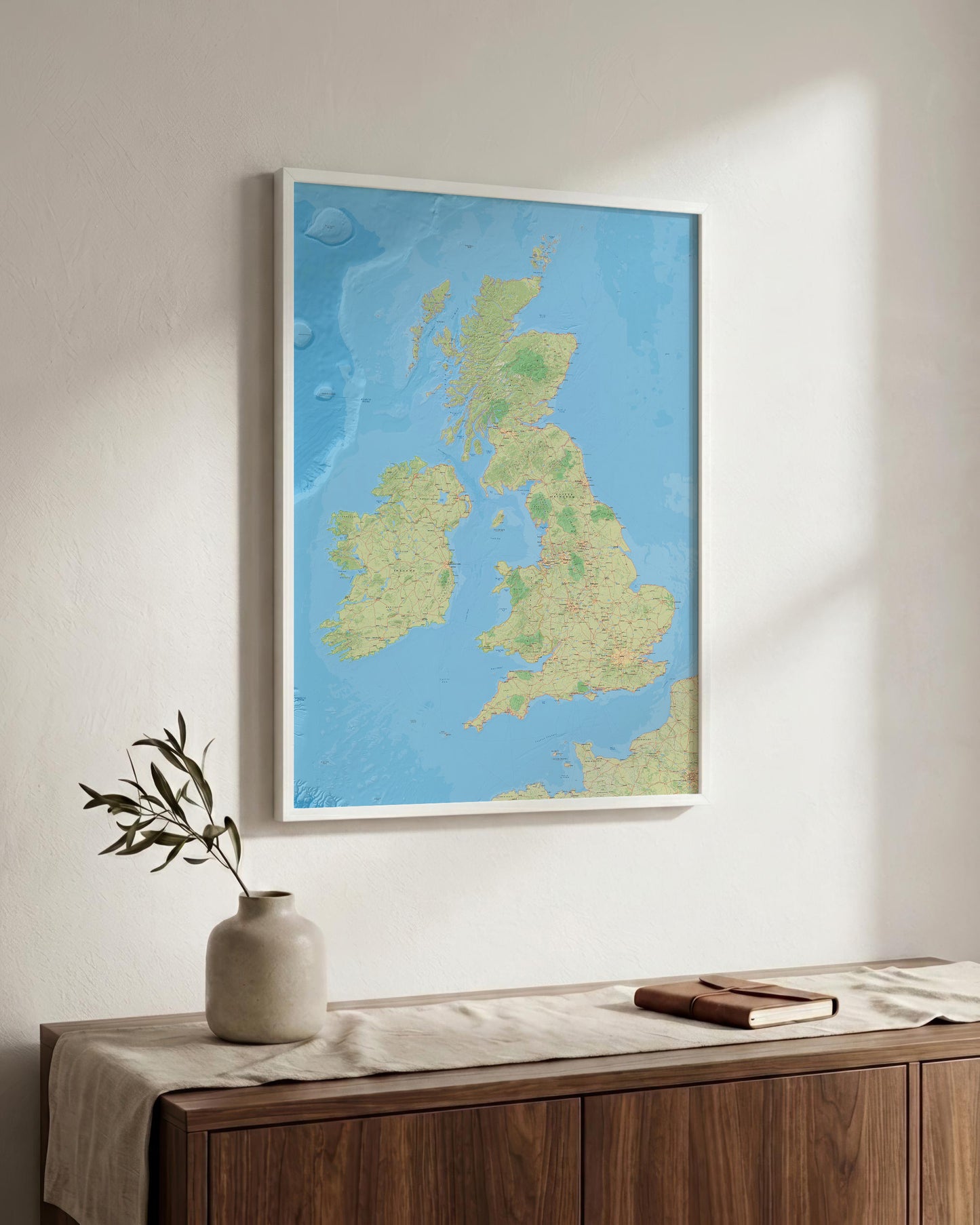 A framed map of the United Kingdom and Ireland hanging on a light-colored wall above a wooden console table with a vase and a book.