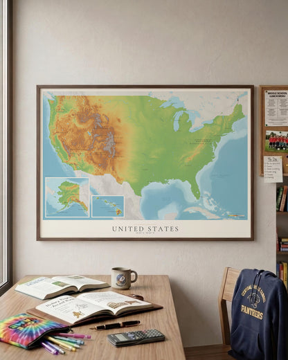A framed United States topographic map poster hanging on a beige wall above a wooden desk with books, a mug, and stationery. A navy blue 'Jackson State Panthers' hoodie rests on a chair to the right.