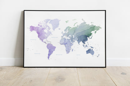 A framed world map art print with a watercolor design in shades of purple, blue, and green on a white background, leaning against a white wall on a light wood floor.