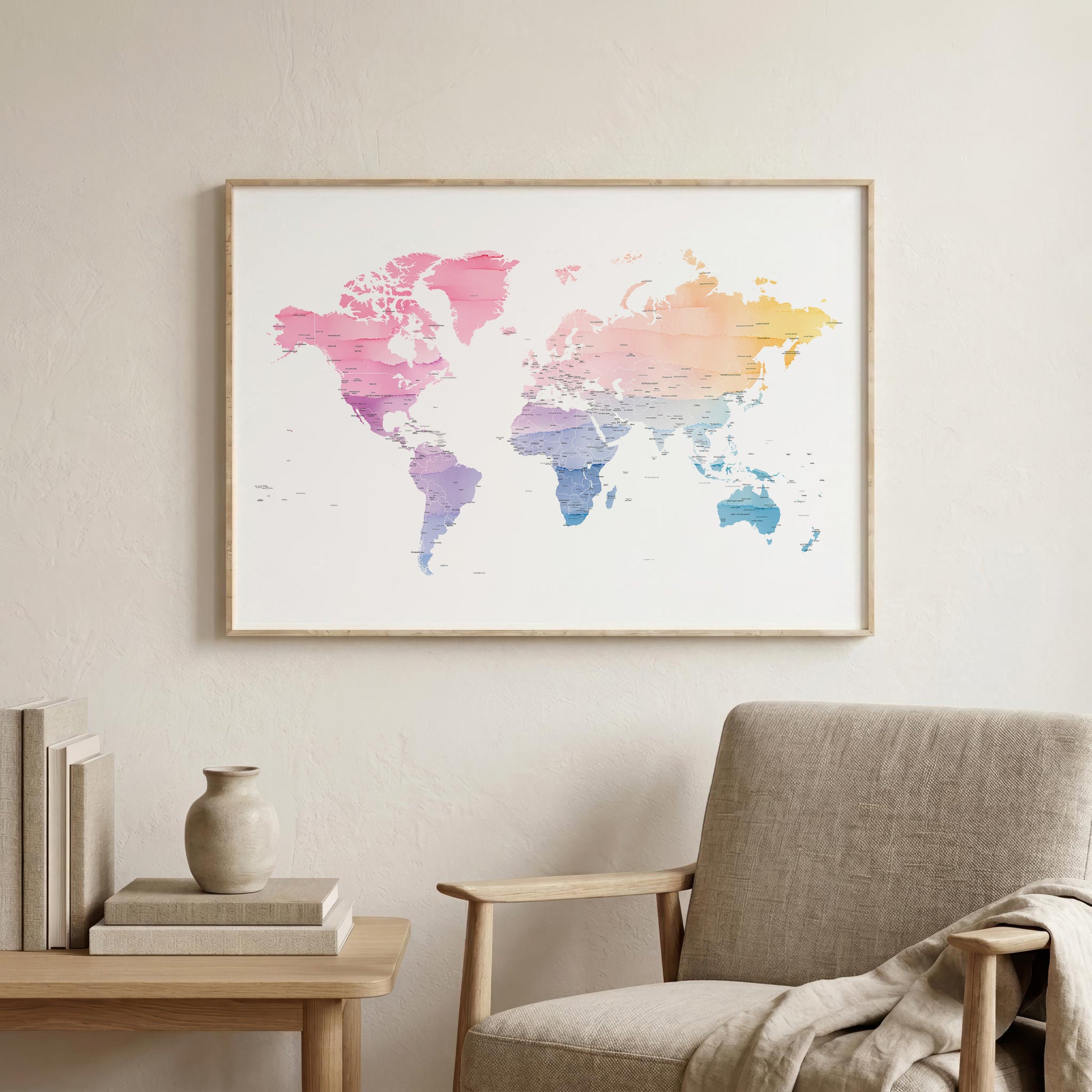 A framed world map art print with a pink, purple, blue, and yellow watercolor gradient, hanging on a light beige wall above a modern armchair and a small side table.