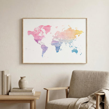 A framed world map art print with a pink, purple, blue, and yellow watercolor gradient, hanging on a light beige wall above a modern armchair and a small side table.