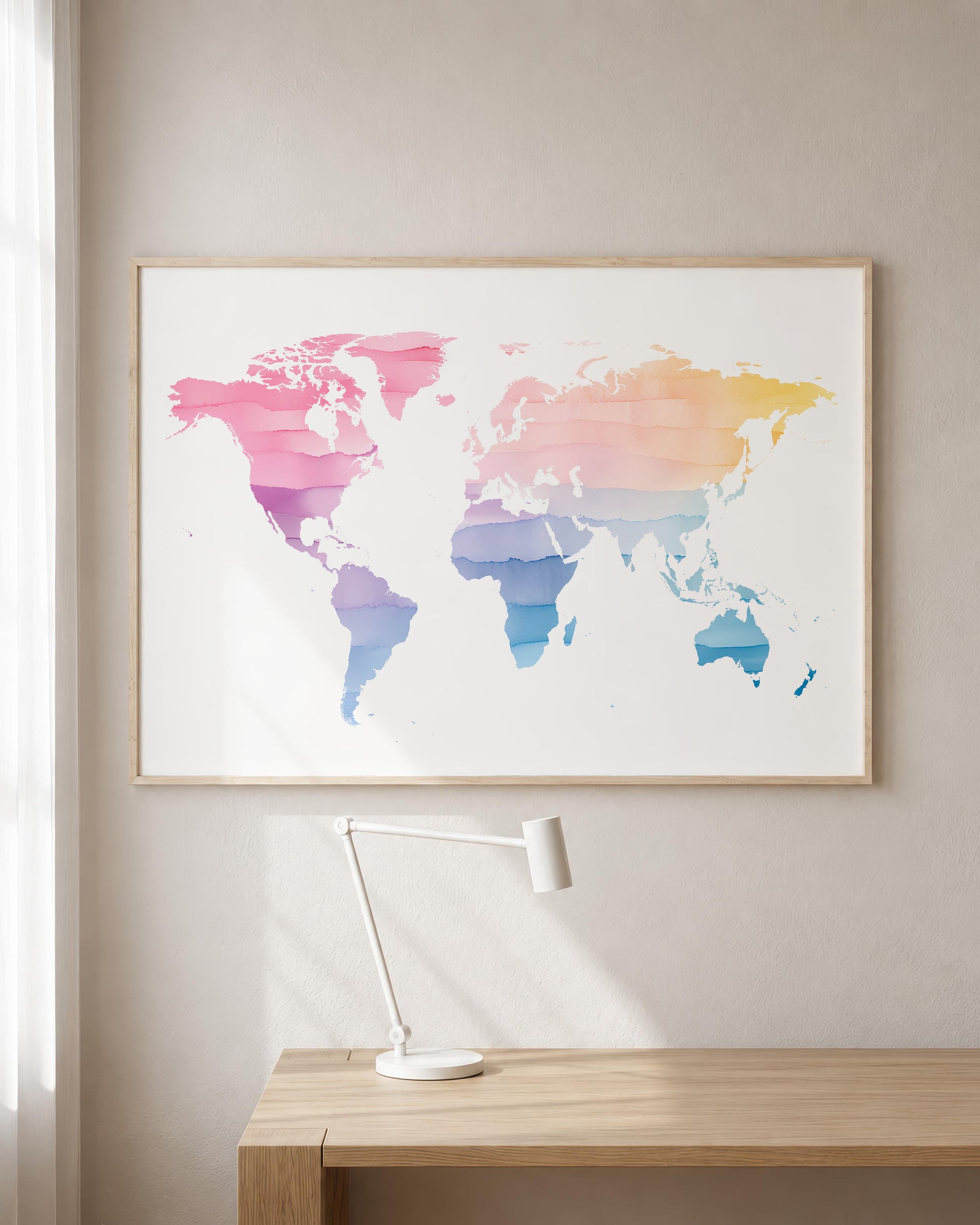 A framed world map art print with a colorful watercolor gradient hangs on a beige wall above a light wood desk with a white desk lamp.