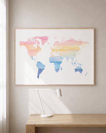 A framed world map art print with pastel watercolor continents in pink, orange, yellow, and blue tones, hanging on a light beige wall above a wooden desk with a white desk lamp.