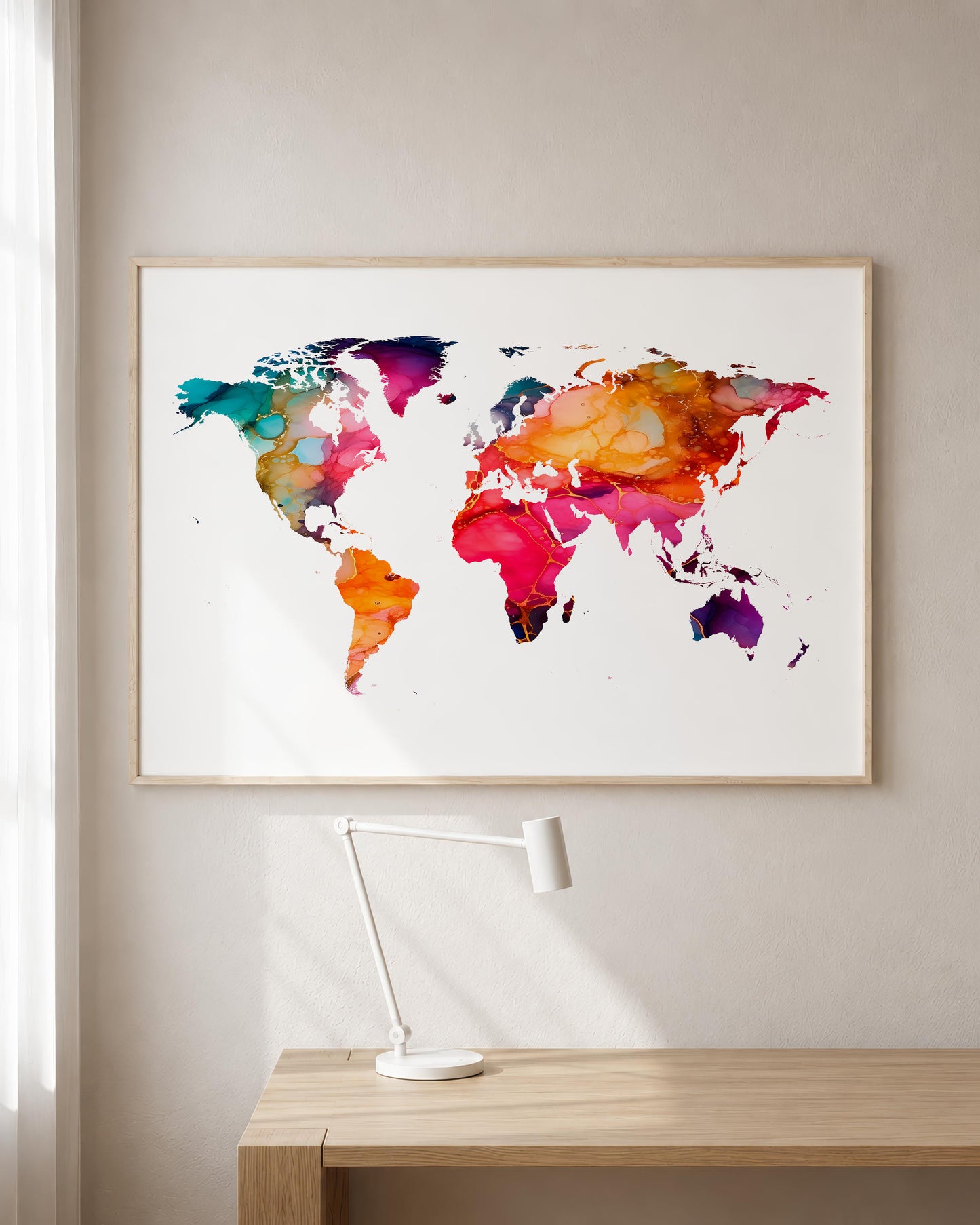 A framed world map watercolor print with vibrant multicolor continents hangs on a light beige wall above a wooden desk with a white desk lamp.