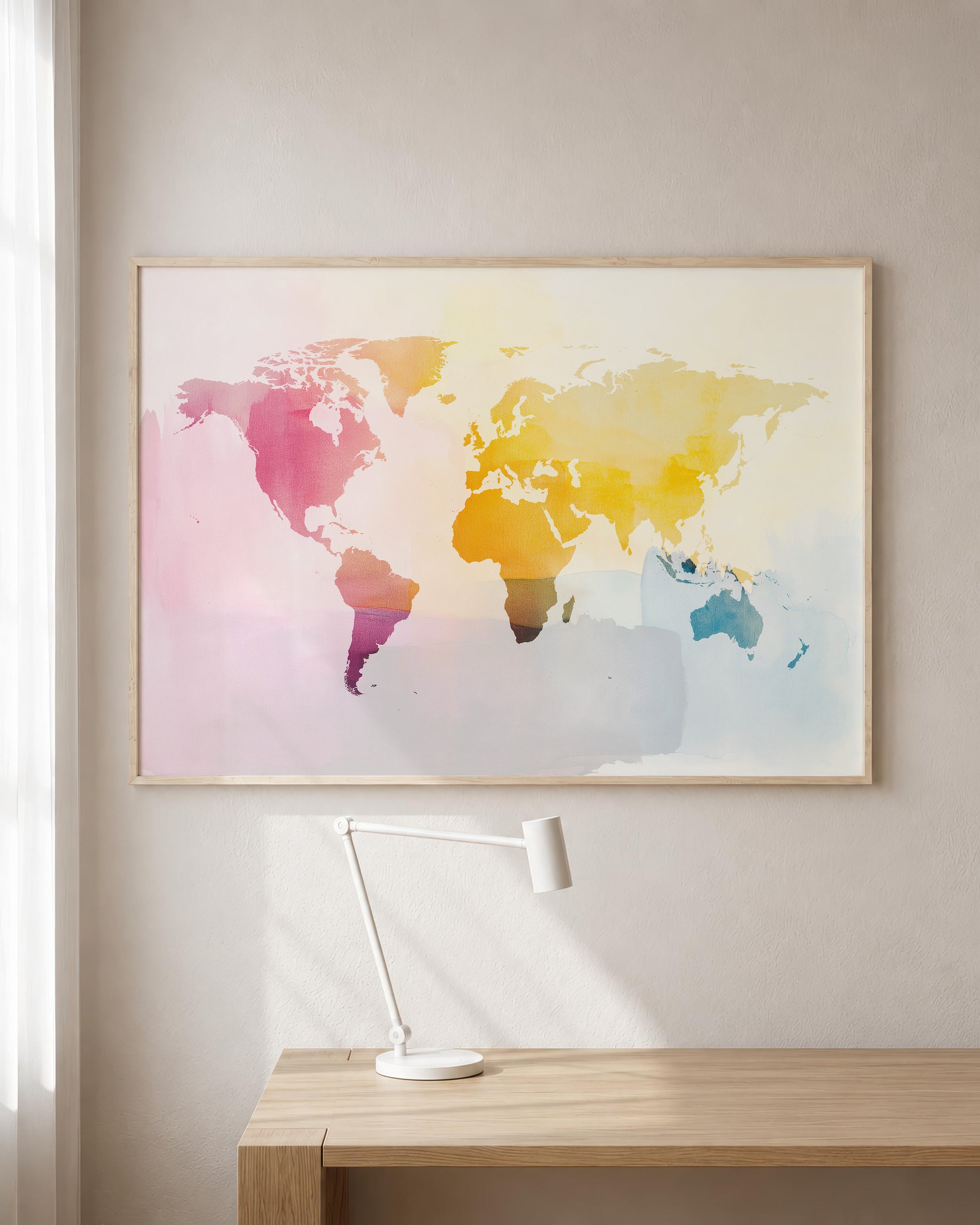 A framed watercolor world map art print hangs on a light beige wall above a wooden desk with a white desk lamp.
