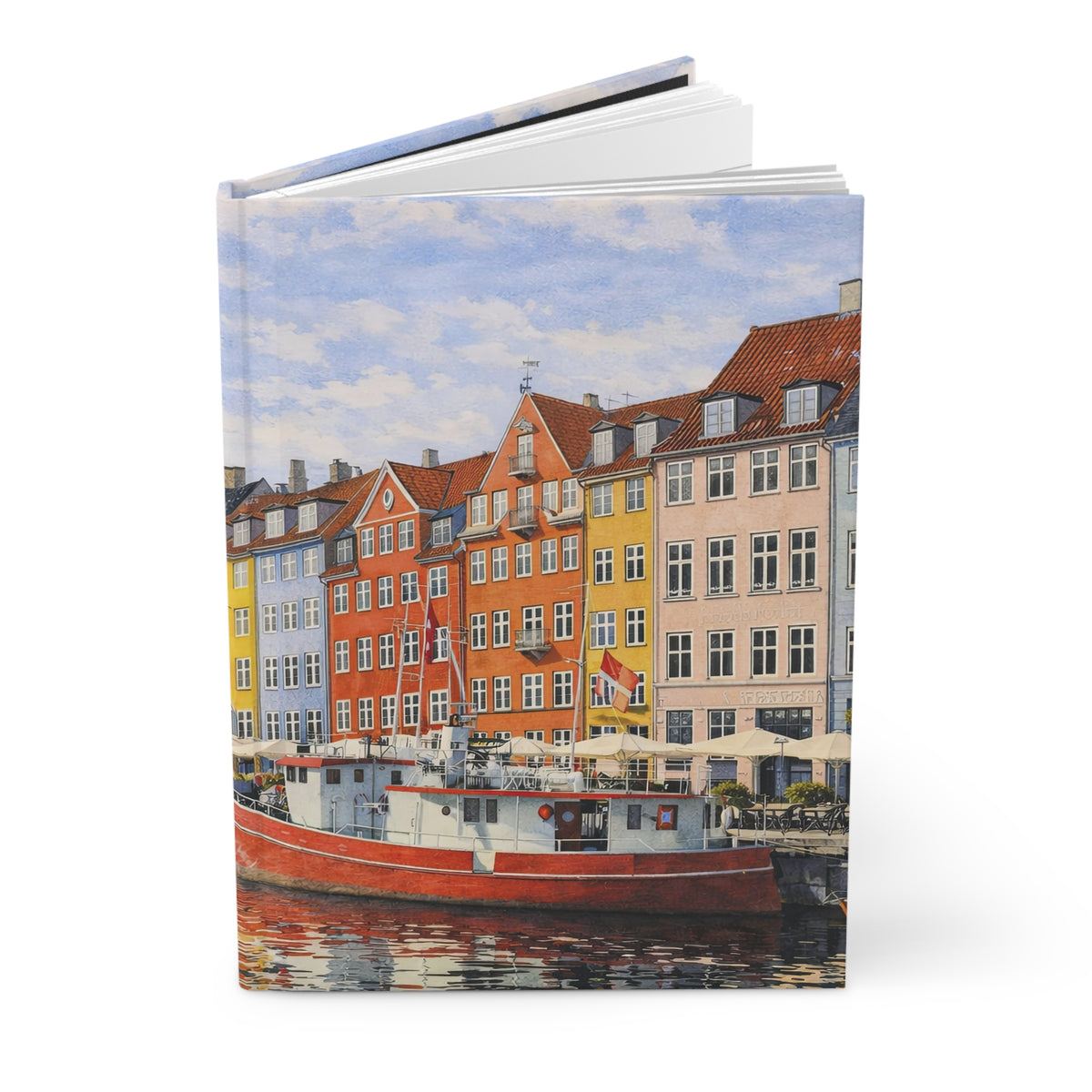 A hardcover book or journal standing upright, printed with a colorful painting of a canal-side row of buildings and a red boat in the foreground, photographed on a clean white background.