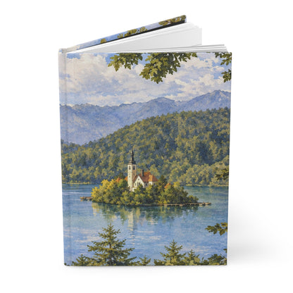 A hardcover notebook or journal standing upright, featuring a scenic landscape illustration on the cover of an island church surrounded by blue water and green mountains, photographed on a clean white background.