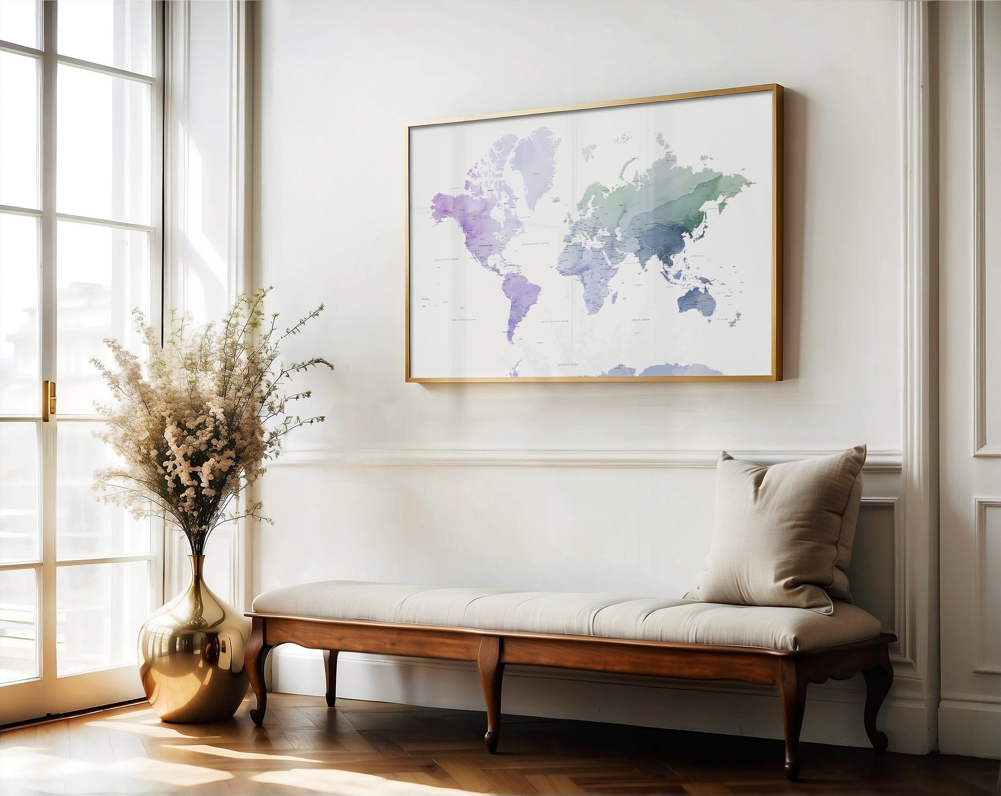 A framed world map art print with watercolor-style purple, blue, and green continents hangs on a white wall above a wooden bench with a beige cushion in a bright, sunlit room.