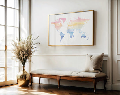 A framed world map art print with a gold frame hangs on a white wall above a wooden bench with a beige cushion in a bright, sunlit room.