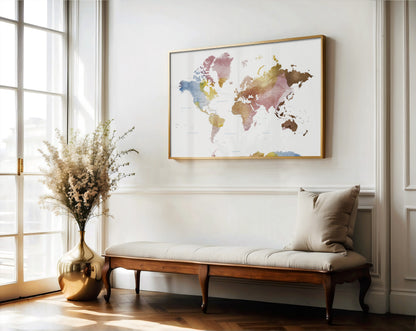 A framed world map wall art print hangs above a wooden bench with a beige cushion in a bright, modern room with a window and a vase of dried flowers.