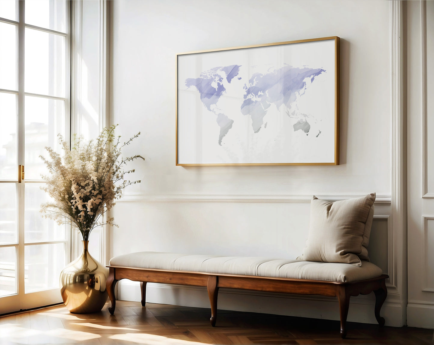 A framed world map print with a gold border hangs on a white wall above a wooden bench with a beige cushion in a bright, sunlit room.