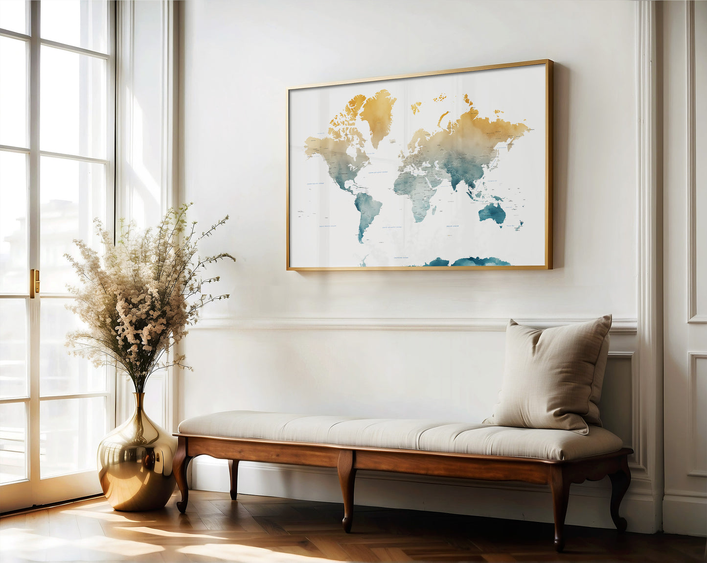 A framed world map art print hangs on a white wall above a wooden bench with a beige cushion in a bright, modern room with a window and a gold vase of dried flowers.