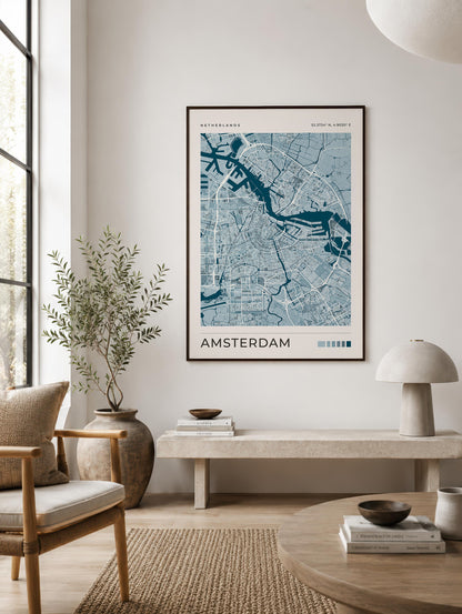 A framed Amsterdam city map poster hangs on a light beige wall in a modern, sunlit living room with a chair, bench, lamp, and rug.