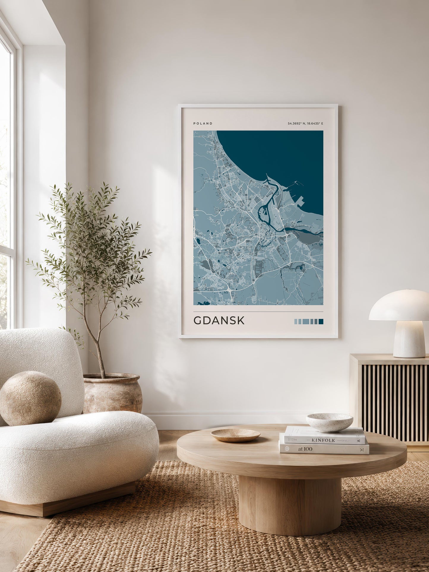 A framed minimalist map poster of Gdansk, Poland, featuring a light blue and white street map with a dark teal coastal area, styled in a modern living room setting.