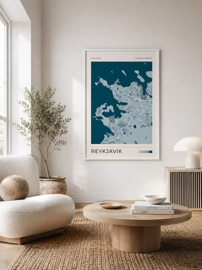 A framed minimalist map print of Reykjavík hangs on a white wall in a modern, sunlit living room with a cream sofa, round wooden coffee table, and a potted plant.