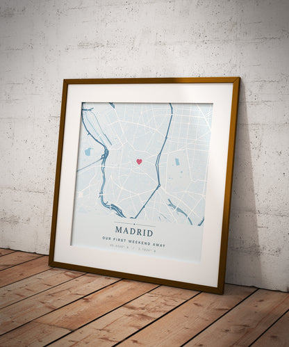 A framed personalized Madrid city map print with a gold frame and white mat, leaning against a white brick wall on a wooden floor.