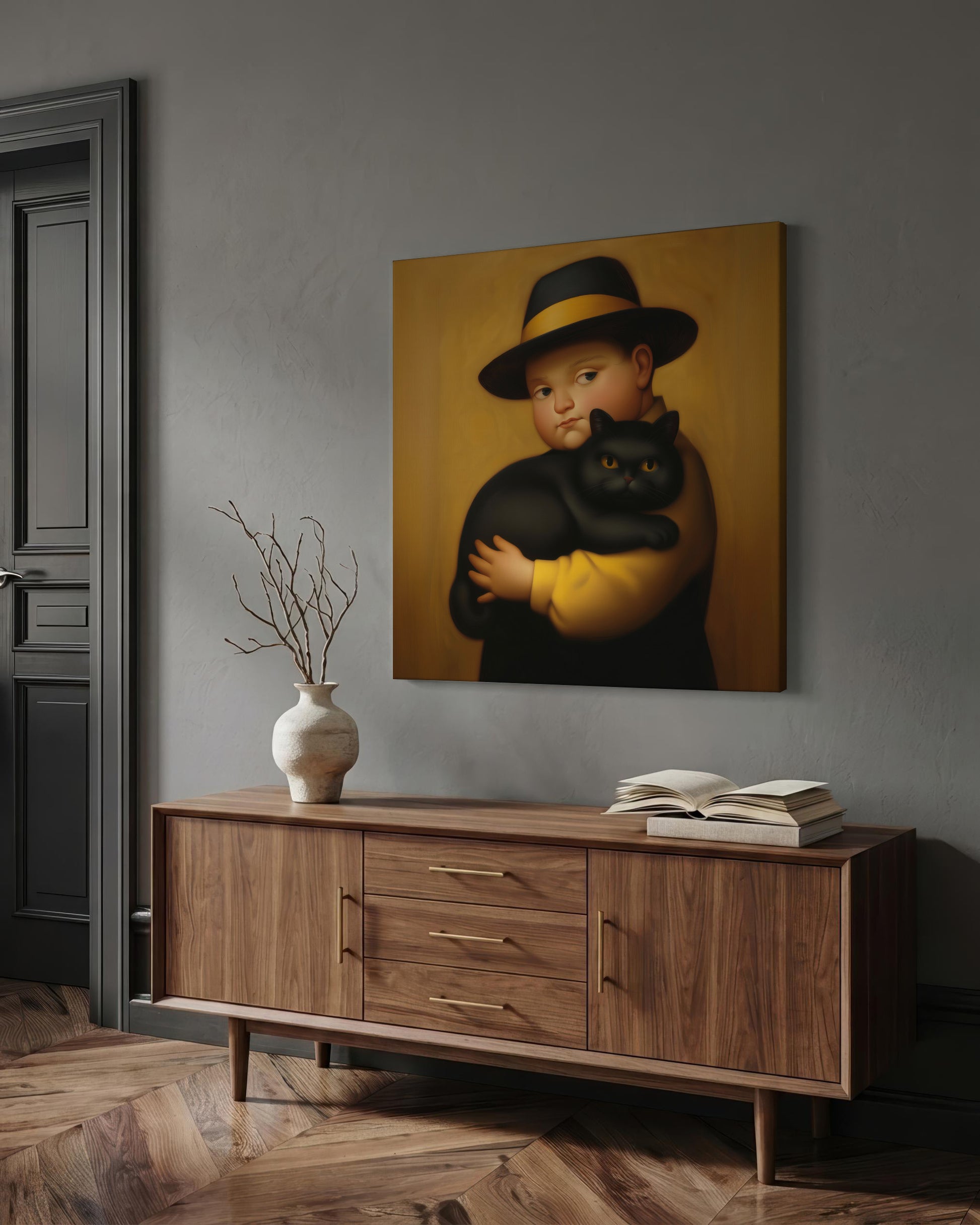 A framed-style wall art print depicting a child in a black hat and yellow shirt holding a black cat, displayed above a wooden sideboard in a styled interior with a vase and books.