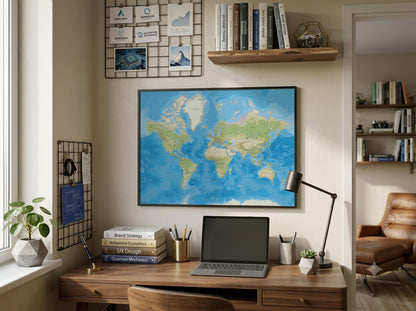 A framed world map poster hangs on a beige wall above a wooden desk in a styled home office setting. The room includes a laptop, desk lamp, books, plants, shelves, and a leather chair visible in the background.