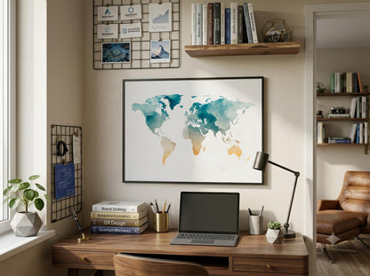 A framed world map art print with teal and gold watercolor continents hanging on a beige wall above a wooden desk in a styled home office setting.