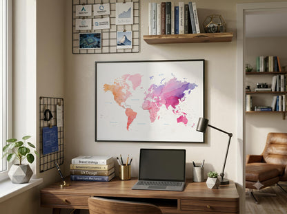 A framed world map poster with a colorful watercolor design hangs on a beige wall above a wooden desk in a styled home office setting.