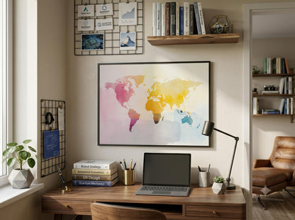 A framed watercolor world map print hangs on a beige wall above a wooden desk in a styled home office. The room includes a laptop, desk lamp, books, plants, shelves, and a chair visible in an adjacent room.