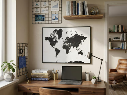 A large black and white world map poster hanging on a beige wall above a wooden desk in a styled home office setting.