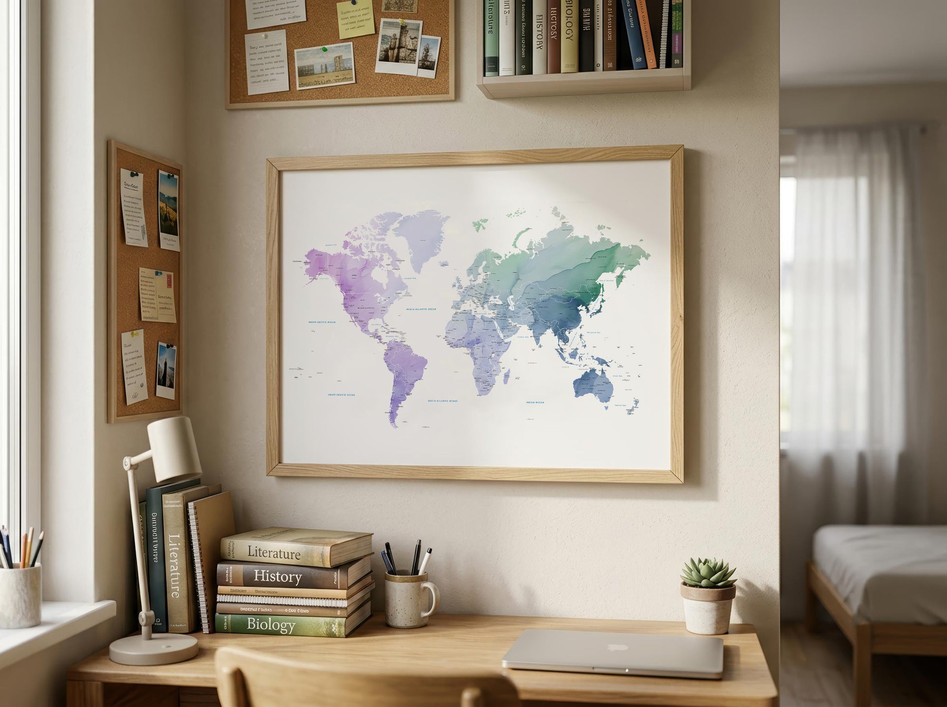 A framed world map poster with a watercolor design in shades of purple, blue, and green, hanging on a beige wall above a wooden desk in a styled home office.