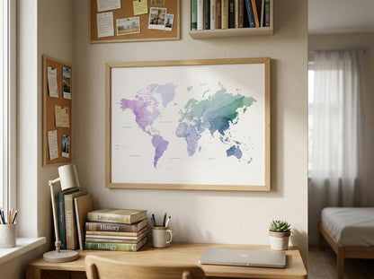 A framed world map poster with a watercolor design in shades of purple, blue, and green, hanging on a beige wall above a wooden desk in a styled home office.