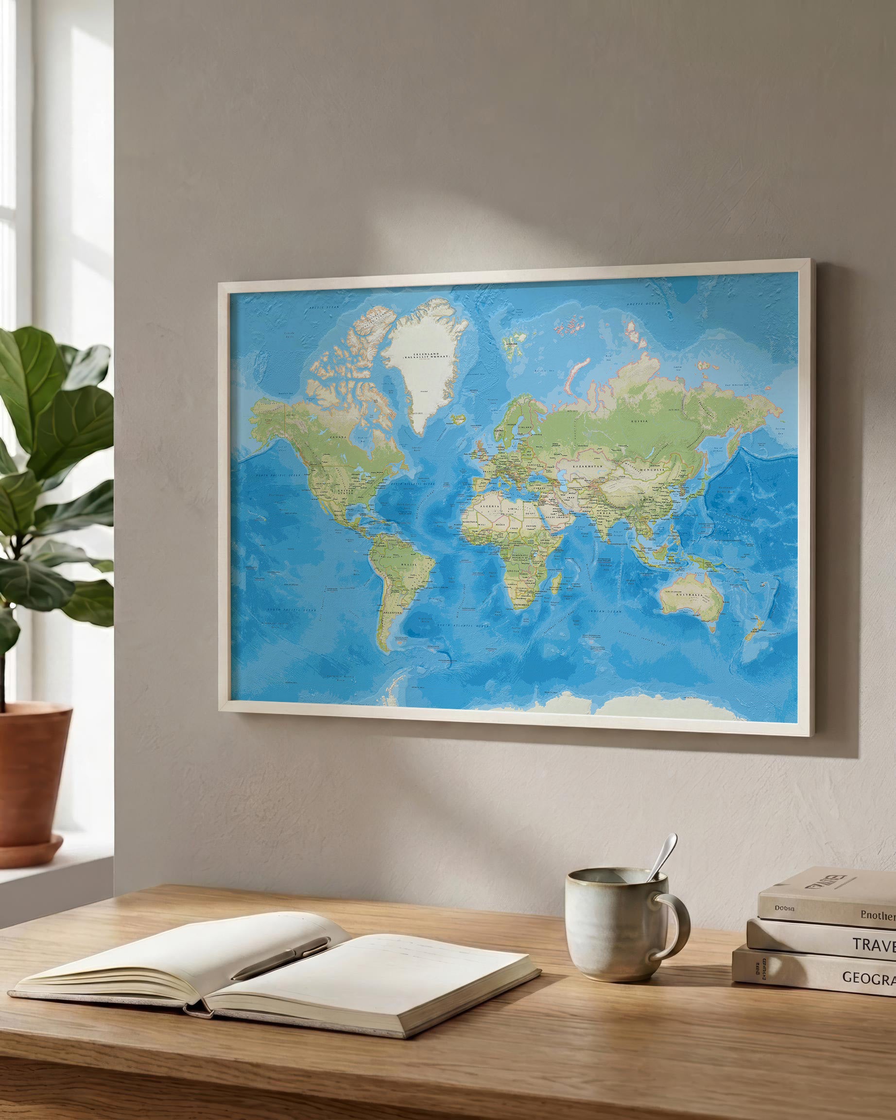 A framed world map print with blue oceans and green landmasses hangs on a beige wall above a wooden desk with an open notebook, a mug, and stacked books.