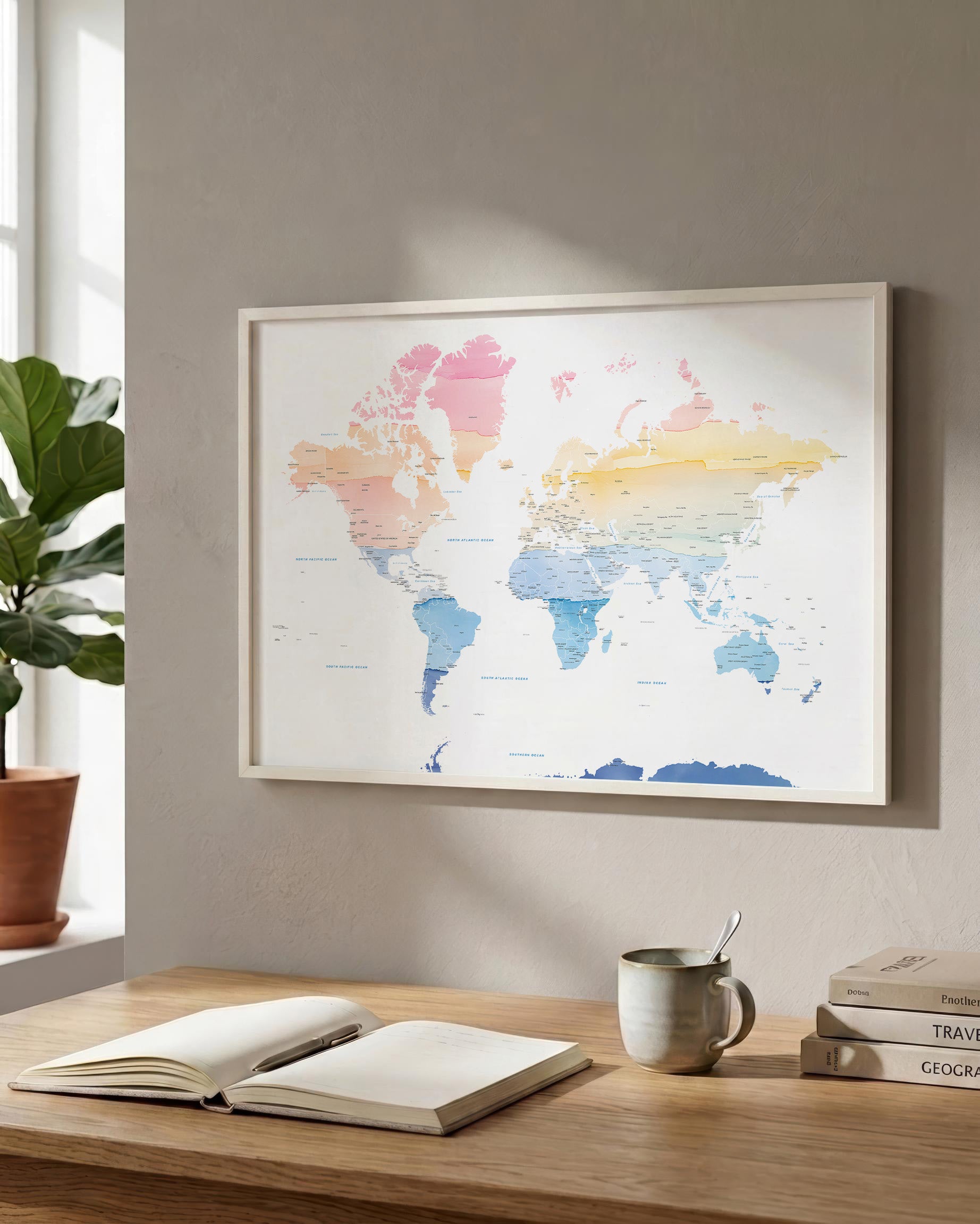 A framed world map poster with pastel watercolor continents hangs on a beige wall above a wooden desk with an open book, a mug, and stacked books.