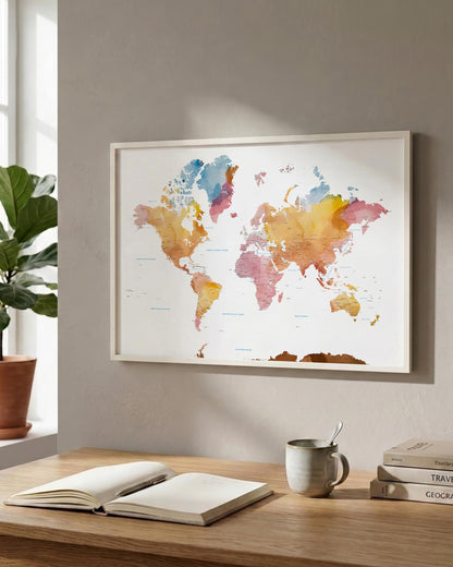 A framed world map poster with a colorful watercolor design hangs on a light gray wall above a wooden desk with an open book, a mug, and stacked books. A potted plant is visible on the left.