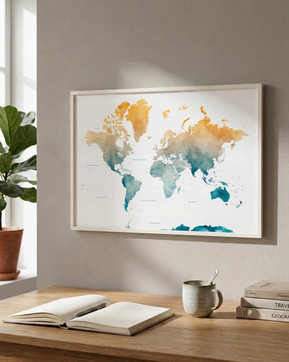A framed world map poster with watercolor-style continents in orange, yellow, teal, and blue tones, hanging on a beige wall above a wooden desk with an open notebook, mug, and books.