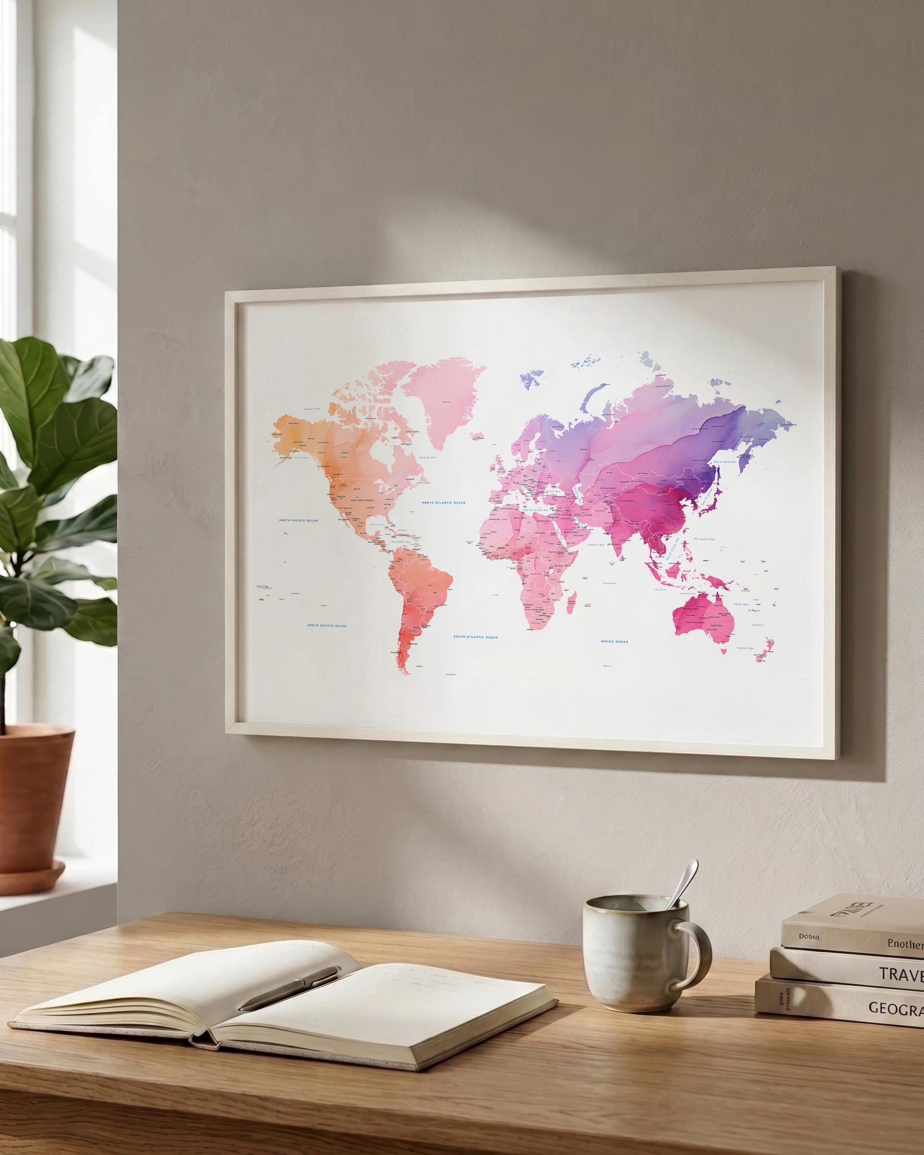 A framed world map poster with a colorful watercolor design hangs on a beige wall above a wooden desk with an open book, a mug, and stacked books.
