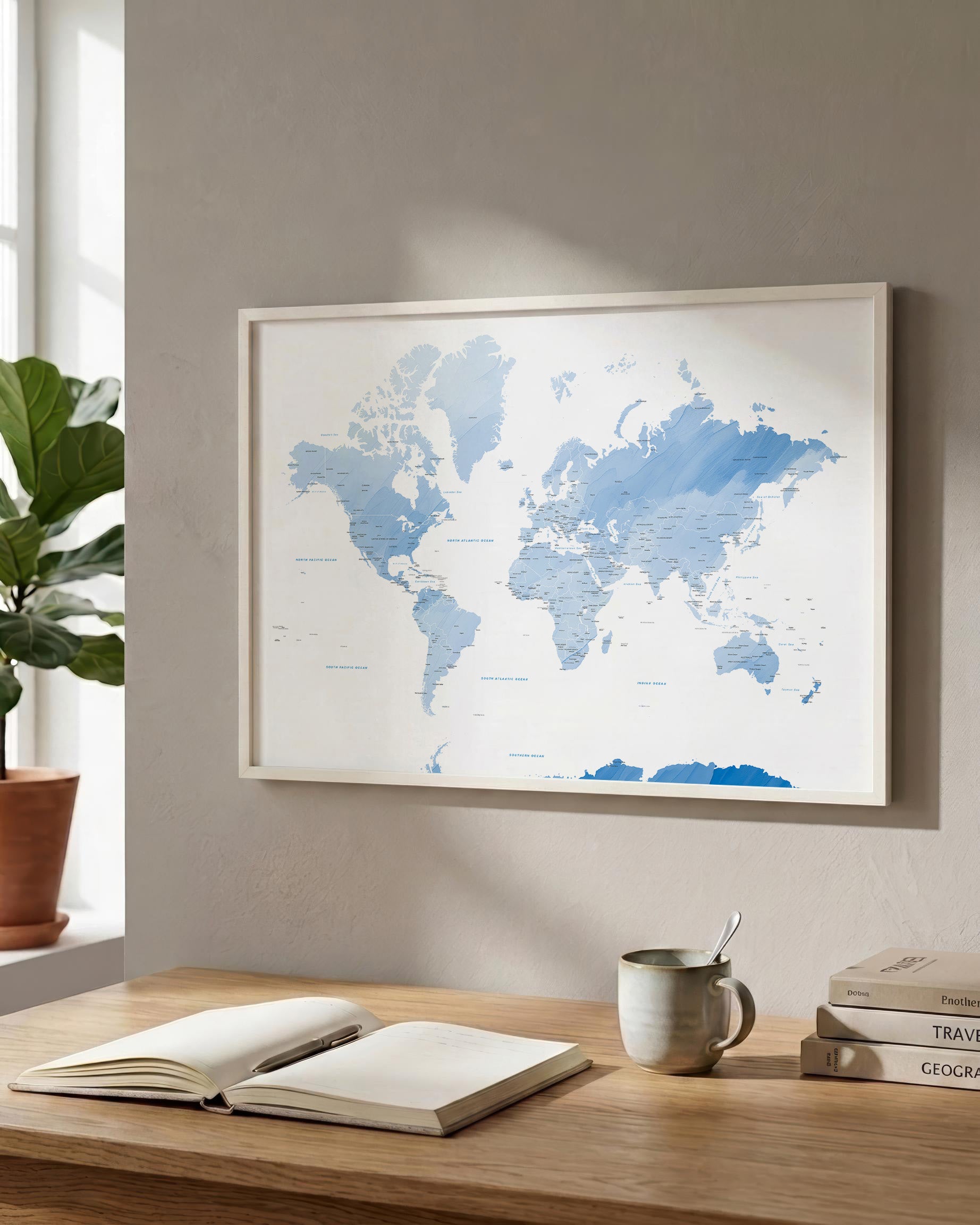 A framed world map print in shades of blue hangs on a light gray wall above a wooden desk with an open book, a mug, and stacked books. A potted plant is visible at the window on the left.