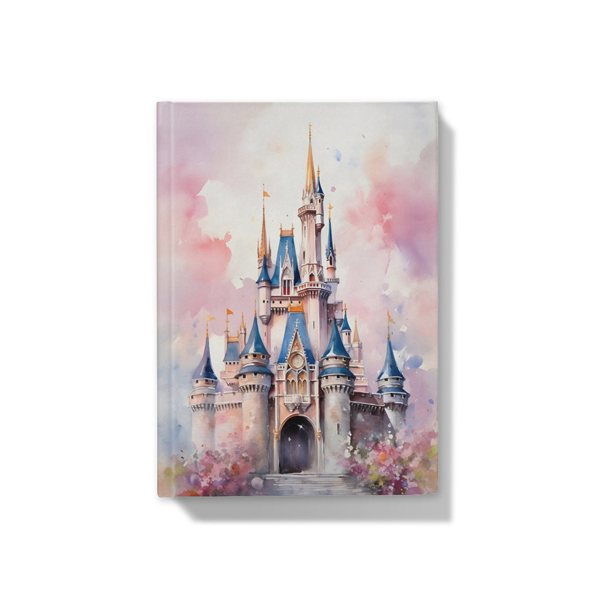 A person holds a notebook featuring a pastel watercolor illustration of a castle, resting on a cozy beige knit blanket on a wooden table with a cup of tea nearby.