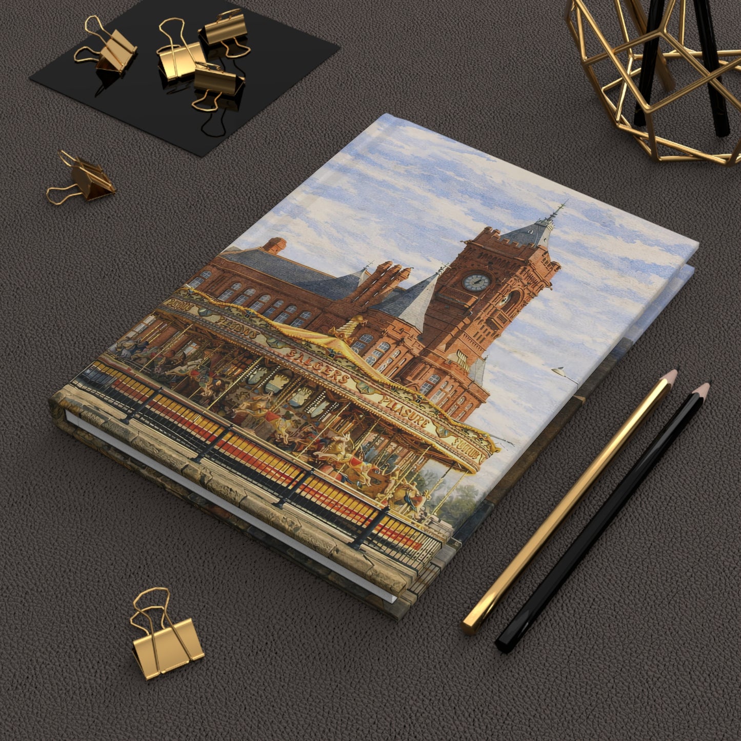 Notebook with a decorative cover featuring a Cardiff cityscape on a dark surface with office supplies.