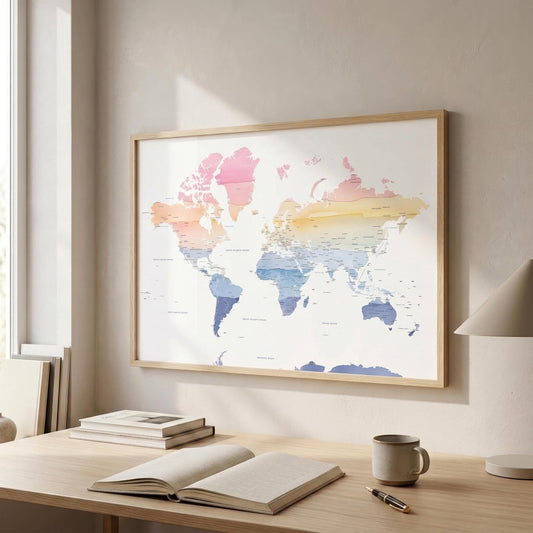 A framed world map poster with pastel watercolor continents hangs on a beige wall above a wooden desk with an open book, notebook, mug, and lamp.