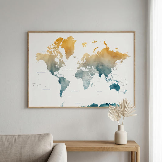 A framed world map wall art print hangs on a light gray wall above a wooden console table with a vase of dried leaves. The map features watercolor-style continents in gold, orange, and teal on a white background, enclosed in a thin natural wood frame.