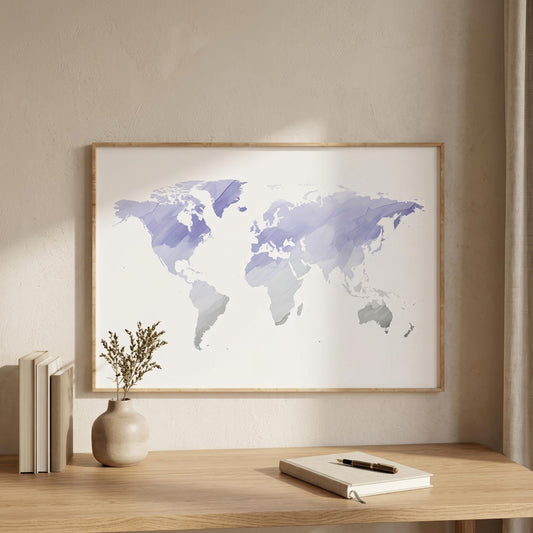 A framed world map art print with watercolor-style purple and blue continents on a white background, displayed on a light wood wall above a wooden desk with books, a vase, and a notebook.
