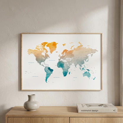 A framed world map art print with a watercolor gradient in orange, yellow, and teal on a white background, hanging on a textured beige wall above a wooden console table with a vase and a book.