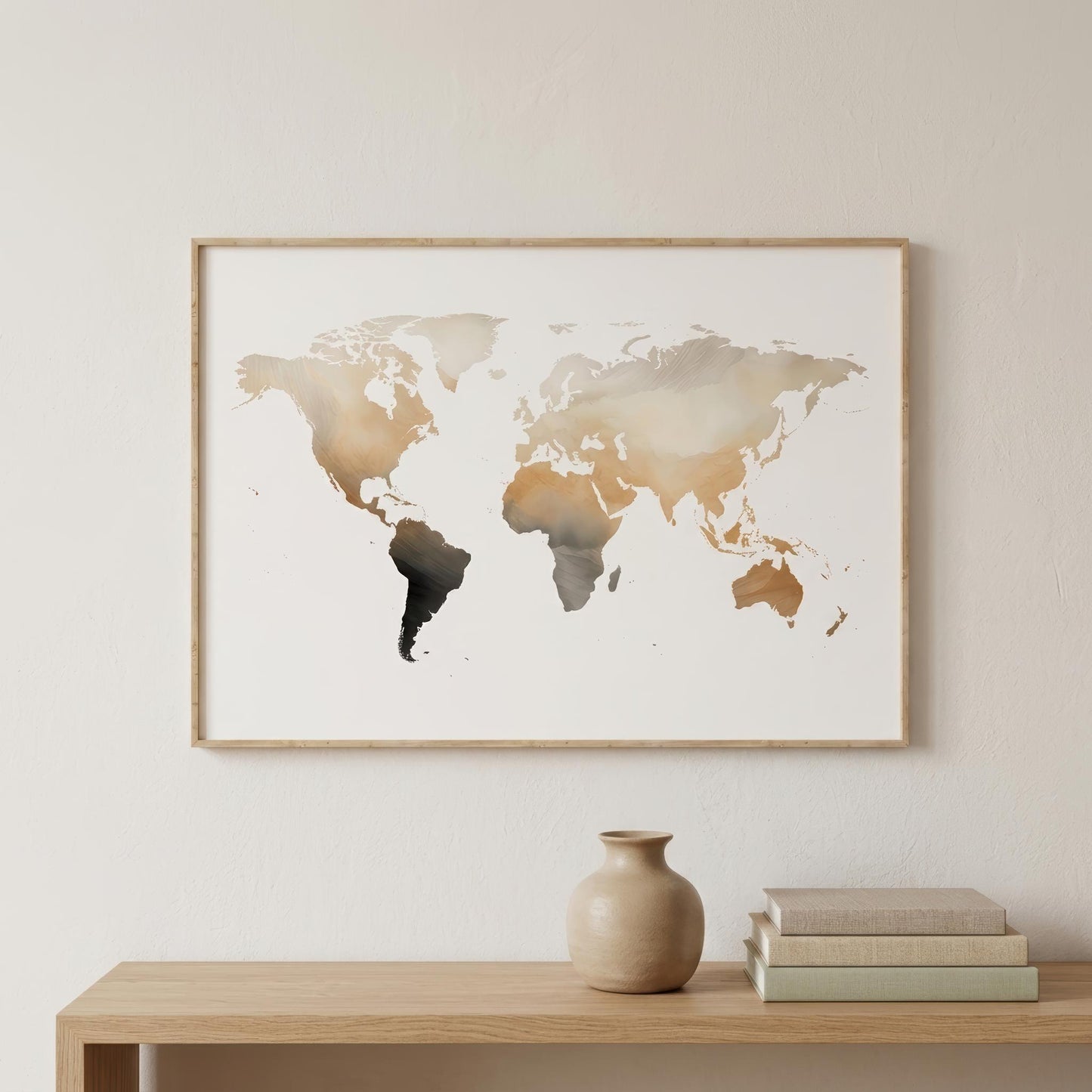 Framed world map wall art with a watercolor-style finish in beige, brown, and black tones, hanging on a light wall above a wooden console table with a vase and books.