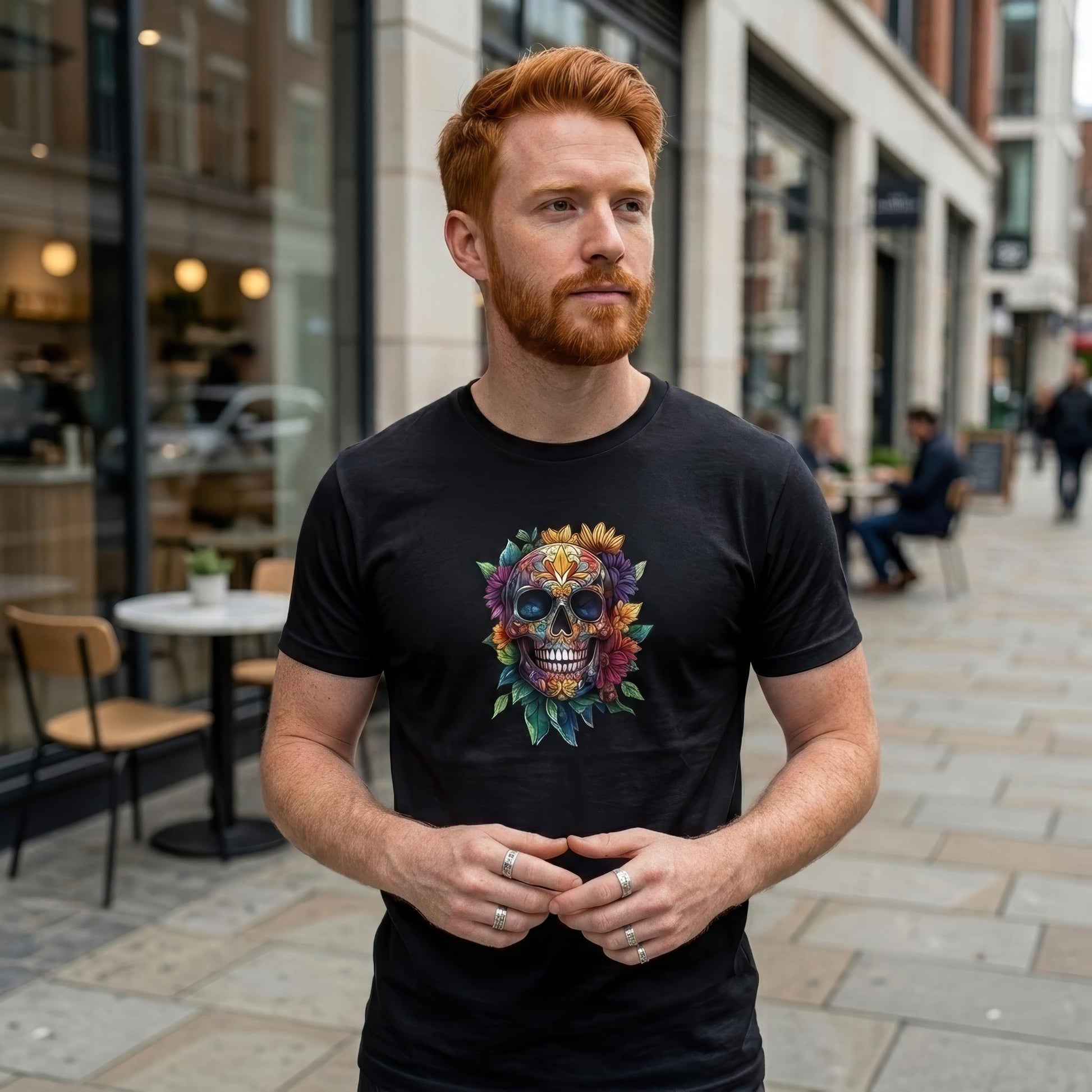 A man with red hair and a beard wearing a black t-shirt with a colorful floral sugar skull graphic, standing on a city sidewalk.