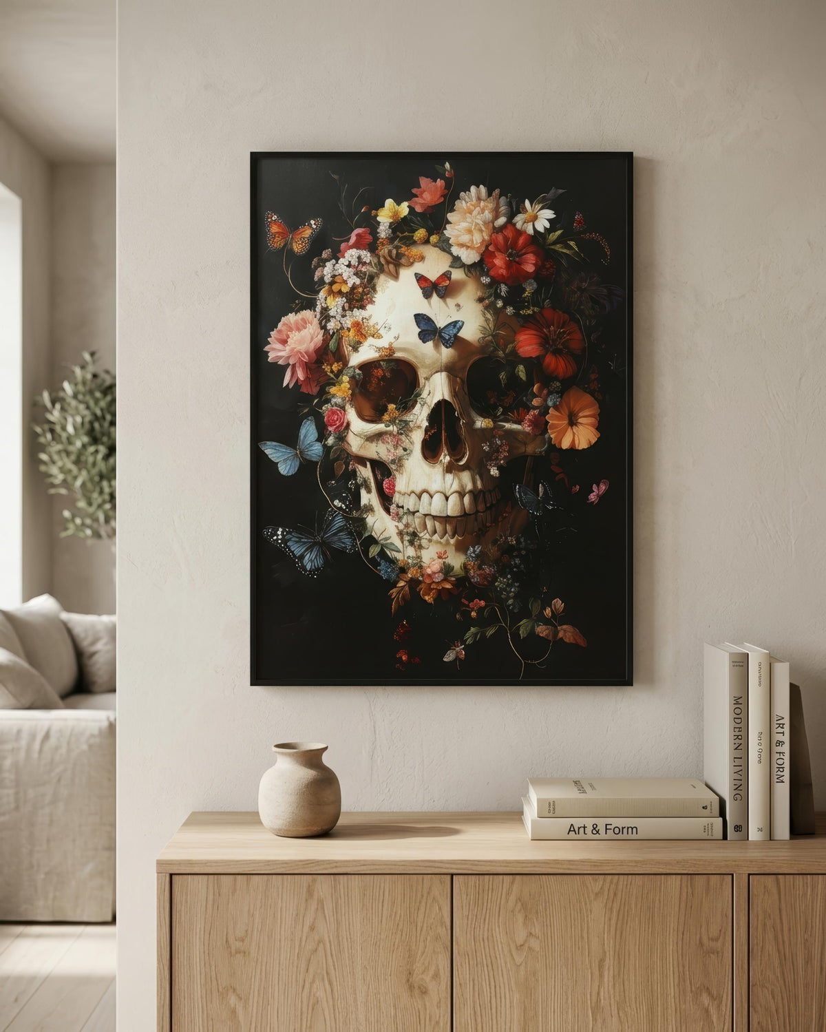 A framed wall art print featuring a detailed skull surrounded by colorful flowers and butterflies on a dark background, displayed in a modern living room setting above a light wood console table.