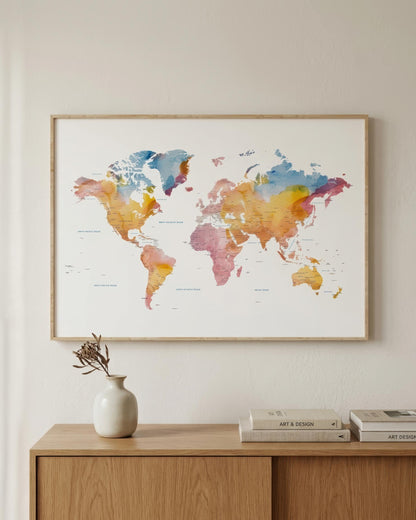 A framed world map watercolor print hangs on a light beige wall above a wooden console table with a small vase and books.