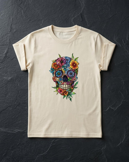 A cream-colored short-sleeve t-shirt with a colorful sugar skull graphic decorated with flowers, laid flat on a dark textured slate background.