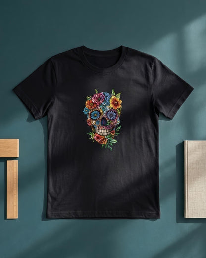 A black short-sleeve crewneck t-shirt featuring a colorful sugar skull graphic with flowers and green leaves, displayed flat against a dark teal background with soft shadows.