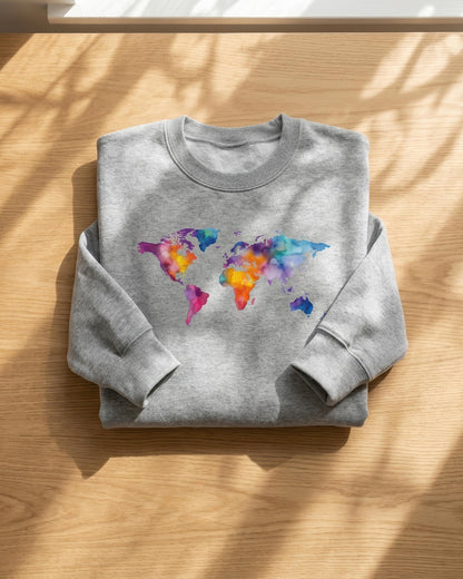 A folded heather gray sweatshirt with a colorful watercolor world map graphic on the chest, displayed on a light wood surface with soft window shadows.