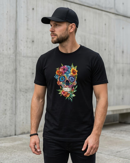 A man wearing a black crewneck t-shirt with a colorful sugar skull graphic, paired with a black baseball cap and black pants, standing against a concrete wall.