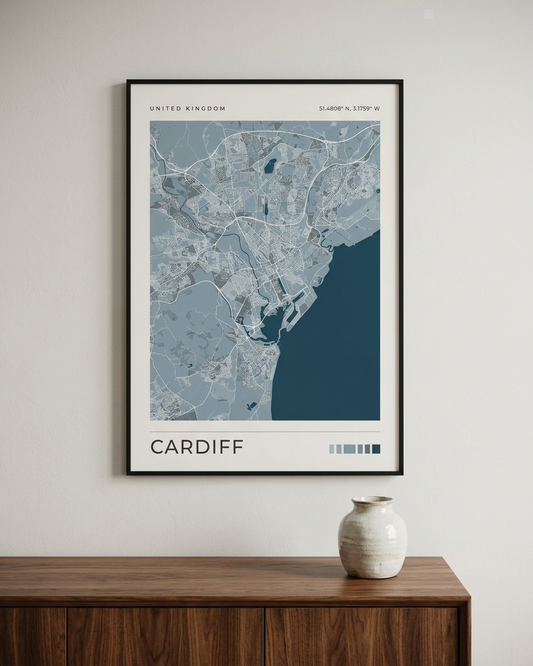 A framed city map print of Cardiff, United Kingdom, displayed on a light gray wall above a wooden console table with a small ceramic vase.
